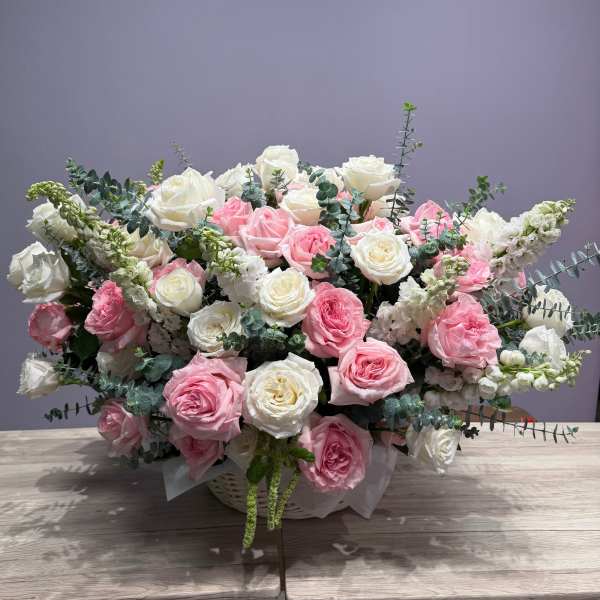 Pink and white rose arrangement in a white basket with eucalyptus