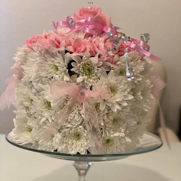 Pink and white flower arrangement on a glass pedestal stand with ribbon bows
