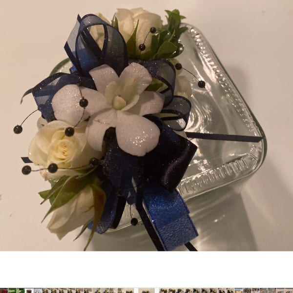 White rose corsage with navy ribbon on a clear tray