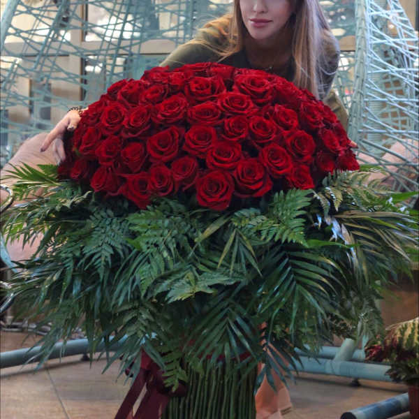 Large bouquet of red roses with dark greenery and ribbon