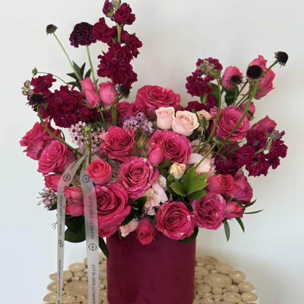 Pink and magenta roses arranged in a round box with ribbon.