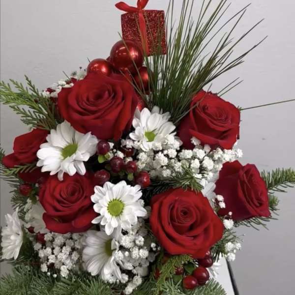 Red roses and white daisies in a festive holiday arrangement with a gift box topper