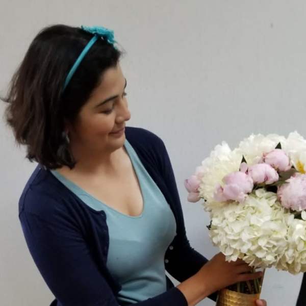 Woman holding a white and pale pink flower arrangement in a gold vase