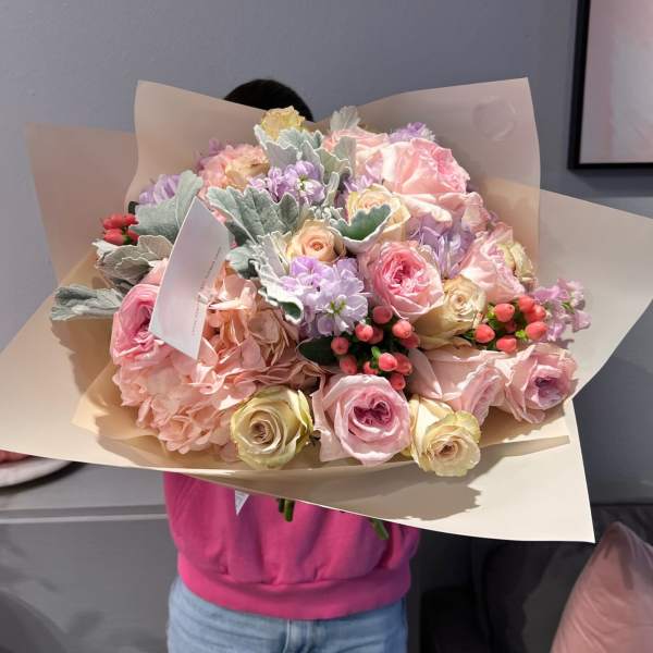 Large pastel bouquet of roses, hydrangeas, and lilac flowers wrapped in beige paper