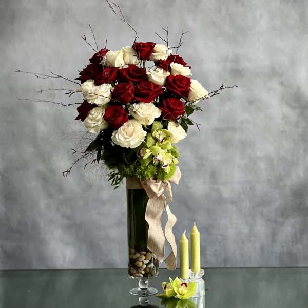 Tall bouquet of red and white roses in a glass vase with ribbon.