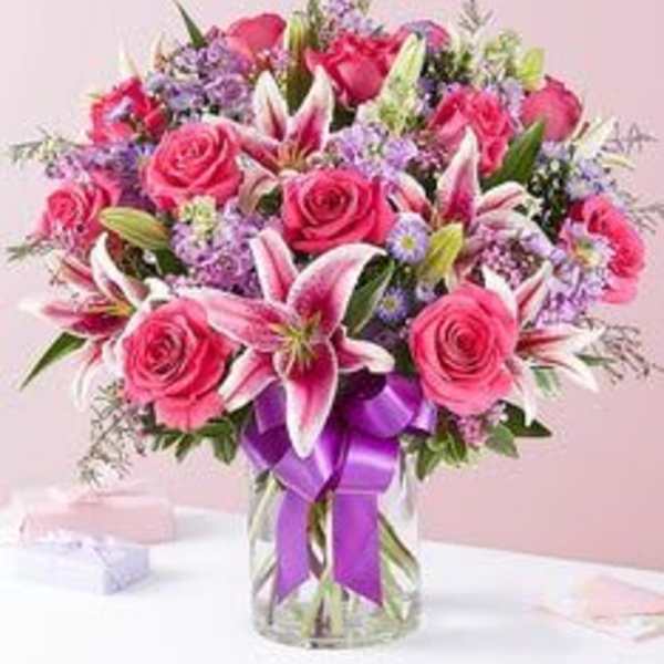 Pink roses and lilies in a glass vase with a purple ribbon