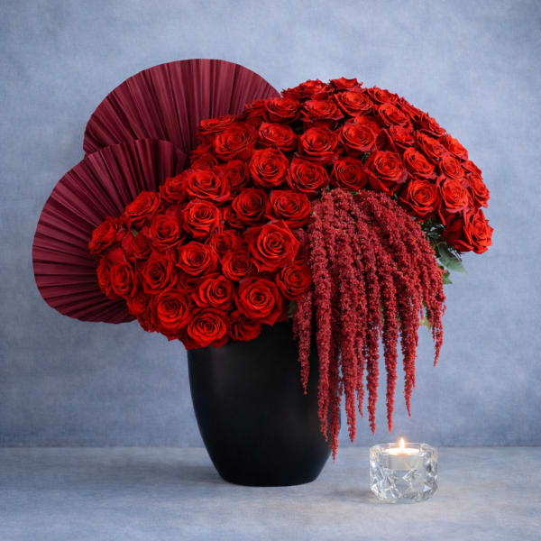 Red rose arrangement in a black vase with burgundy fan accents and a candle