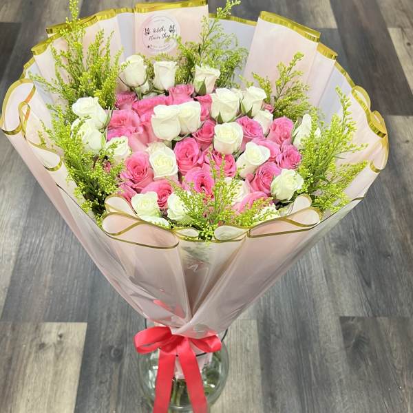 Bouquet of pink and white roses wrapped in pale pink paper with a red ribbon