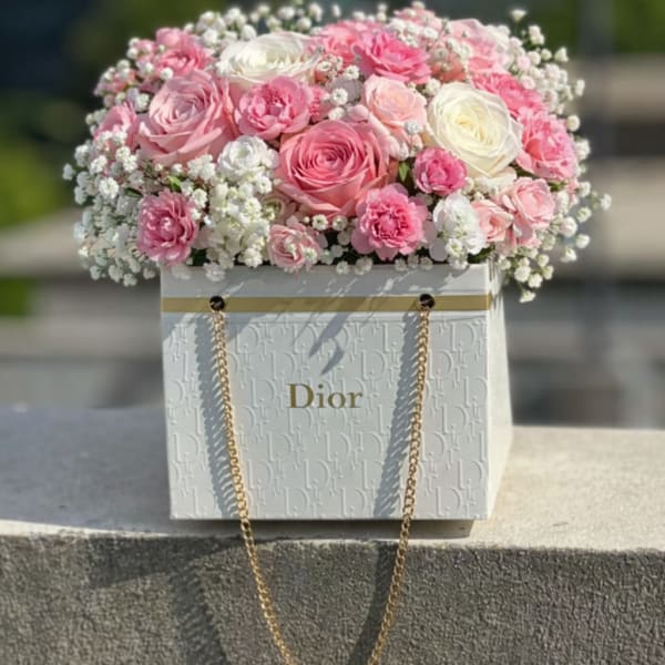 Pink and white roses arranged in a Dior gift box with gold chain handles.