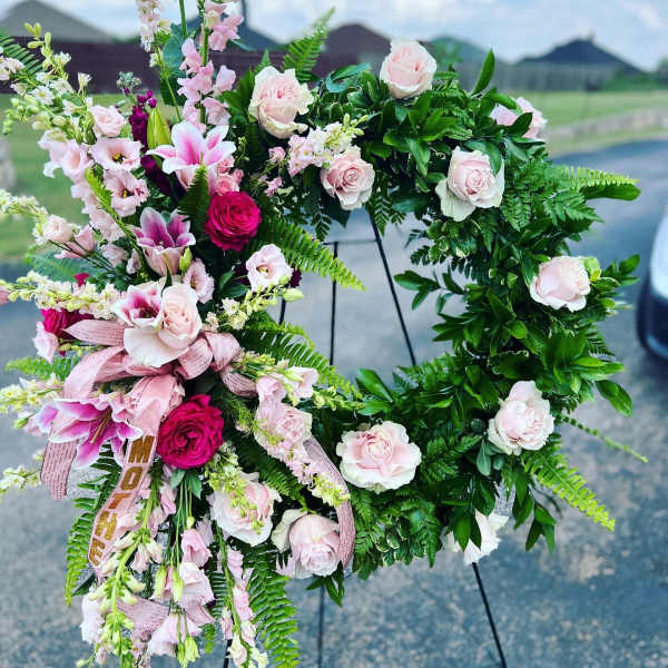 Pink and white floral wreath on a stand with ribbon accents
