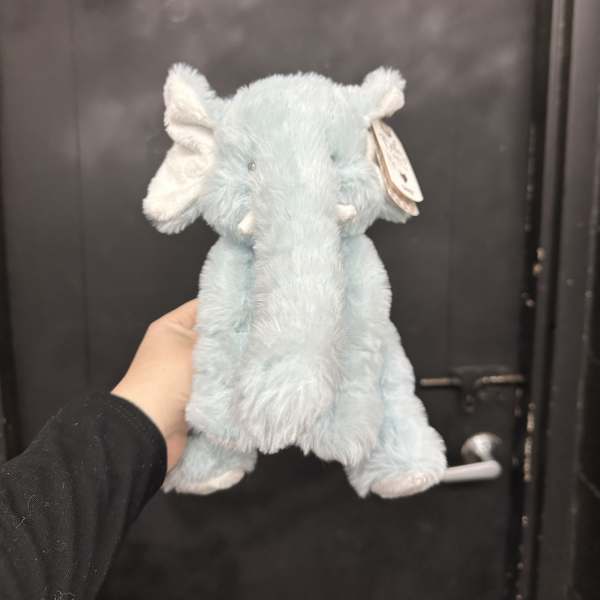Light blue plush elephant toy being held in front of a dark door
