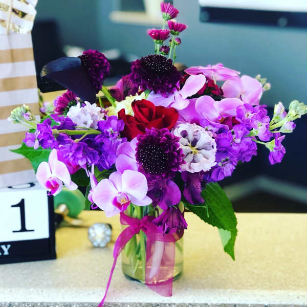 Purple and pink flower arrangement in a glass vase with a red rose