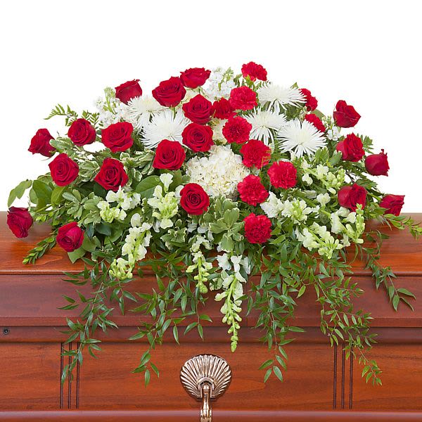 Red and white casket spray with roses, carnations, and mums on a wooden casket