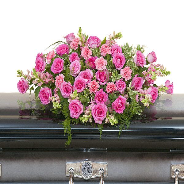 Pink rose and carnation casket spray arranged on top of a dark gray casket