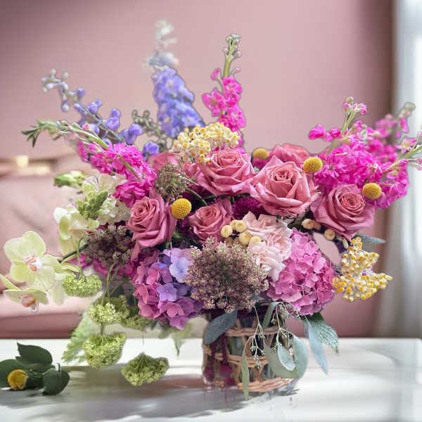 Pink roses and hydrangeas in a woven basket with purple and yellow accents
