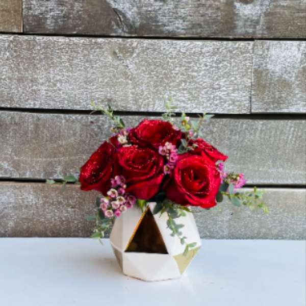 Red roses arranged in a geometric white vase with small pink filler flowers