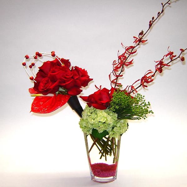 Red roses arranged in a clear glass vase with green hydrangea and decorative branches