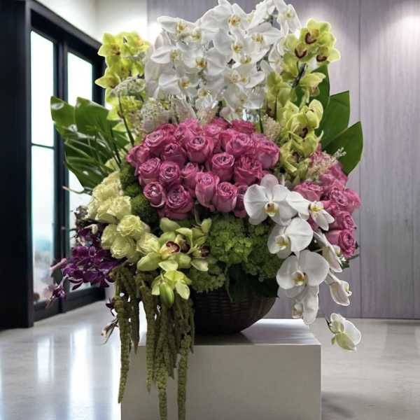 Large arrangement of pink roses and white orchids in a dark bowl