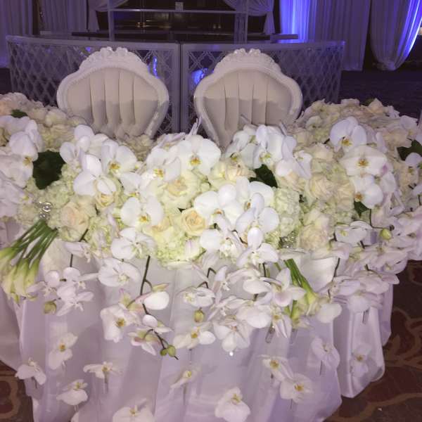 White orchid and rose arrangement on a draped table with two chairs behind it