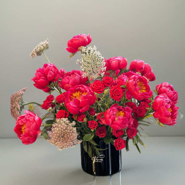 Pink peonies and red roses arranged in a black vase