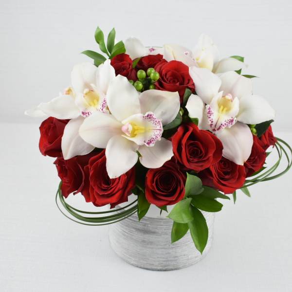 Round arrangement of white orchids and red roses in a low white cylinder vase