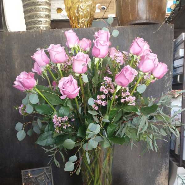 Pink roses arranged in a tall glass vase with eucalyptus and small filler flowers.