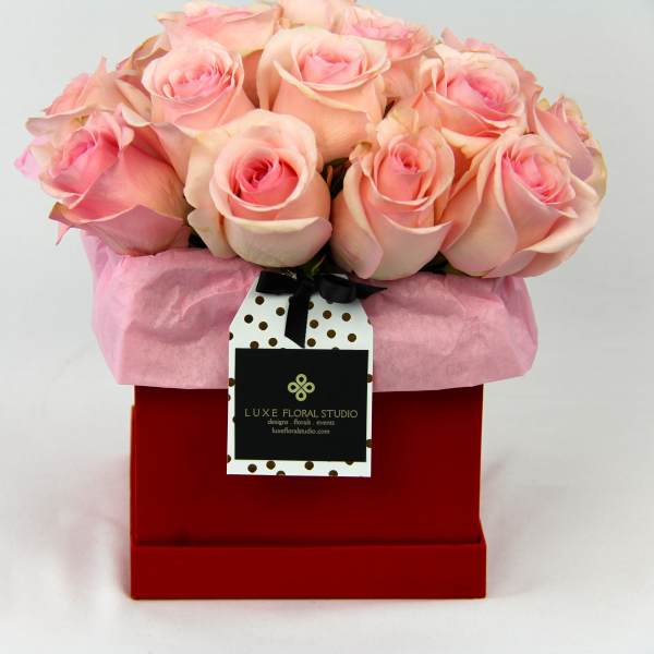 Pink roses arranged in a red gift box with a hanging tag