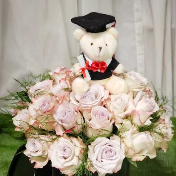 Teddy bear in a graduation cap sitting in a bouquet of pale pink roses
