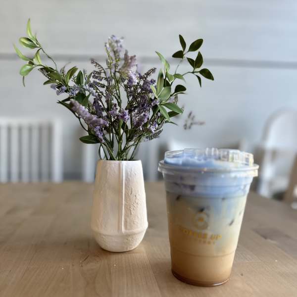 Small purple flower arrangement in a white vase beside an iced drink