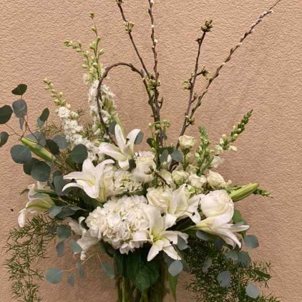 White lilies and hydrangeas in a clear glass vase with tall branches