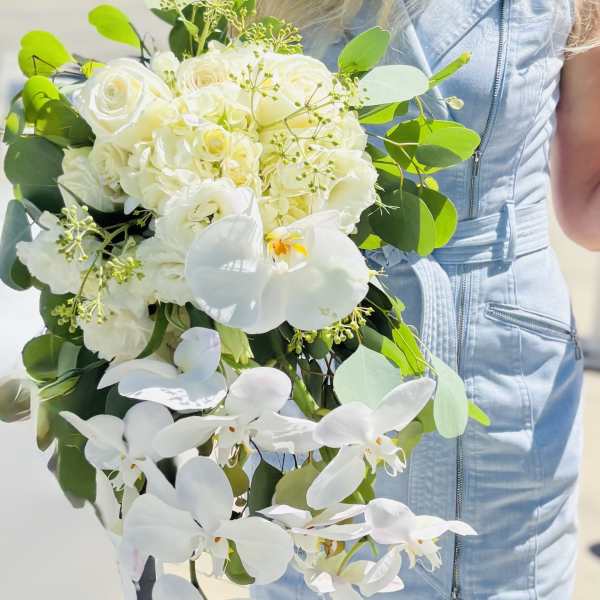 White bouquet with roses and orchids held by a person in a light blue dress