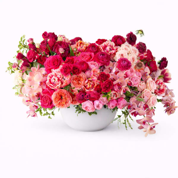 Large pink and red floral arrangement in a white bowl vase