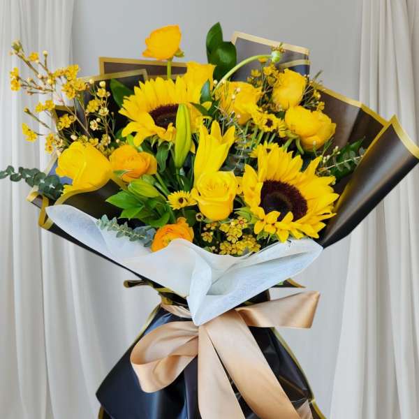 Bouquet of yellow flowers wrapped in black paper with a gold ribbon