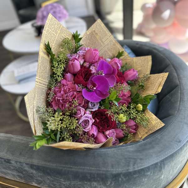 Pink and purple bouquet with roses and orchids wrapped in newspaper-style paper