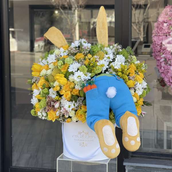 Yellow and white flower arrangement with a plush bunny in a white box