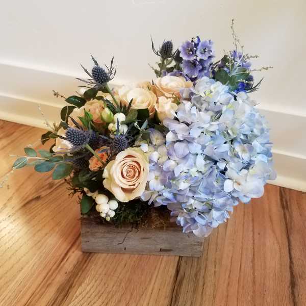 Low wood box arrangement with blue hydrangeas, peach roses, and blue accent flowers
