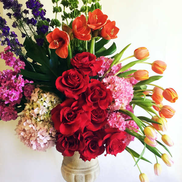 Mixed bouquet of red roses, orange tulips, and pink hydrangeas in a stone vase