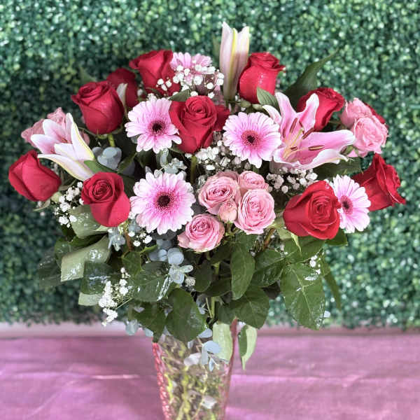 Bouquet of red and pink roses with lilies and pink daisies in a glass vase