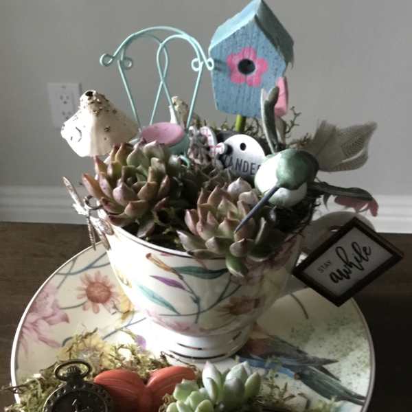 Succulent arrangement in a floral teacup with birdhouse and decorative accents