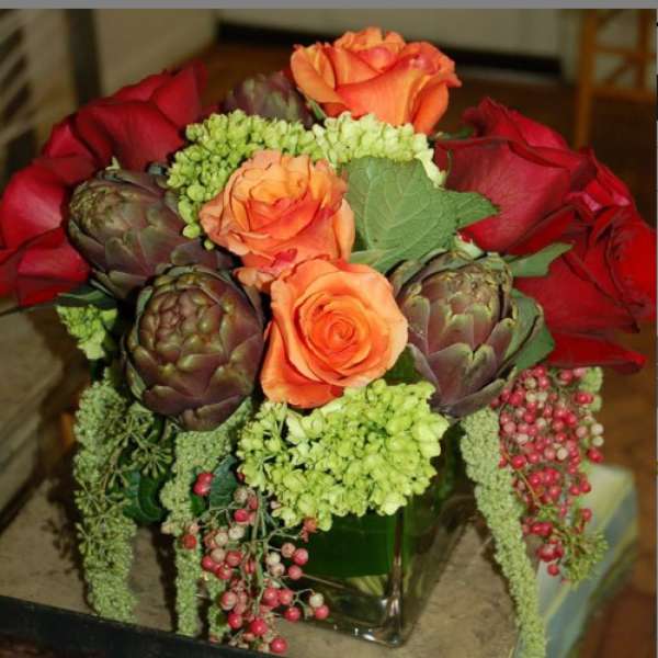 Bouquet of orange and red roses with artichokes in a glass vase