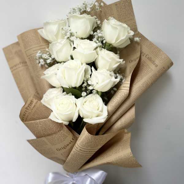 Bouquet of white roses wrapped in brown paper with a white ribbon