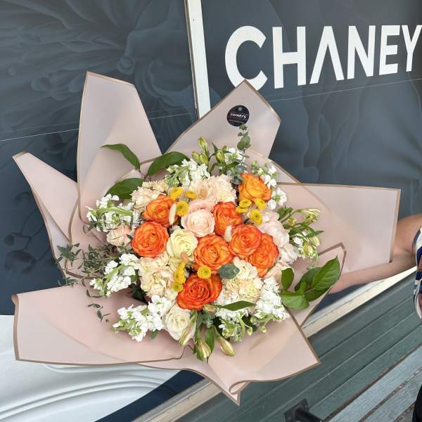 Bouquet of orange and cream roses with white filler flowers in pink wrap