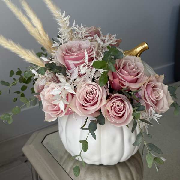 Pink roses arranged in a white pumpkin vase with dried grasses and greenery