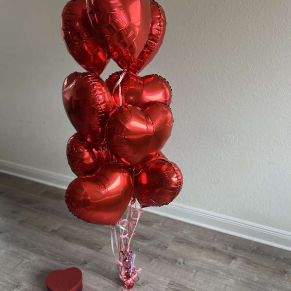 Cluster of red heart-shaped balloons with a small heart gift box on the floor