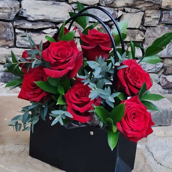 Black gift bag filled with red roses and greenery
