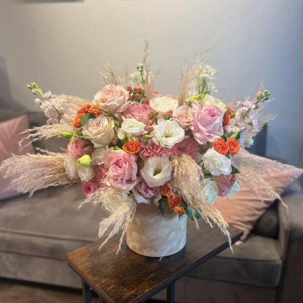 Pink and white rose bouquet in a white vase with dried grasses