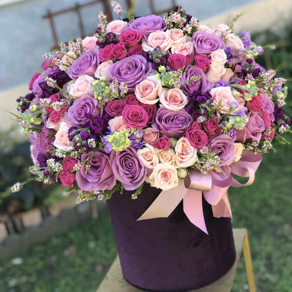 Large bouquet of pink and purple roses in a dark hat box with ribbon