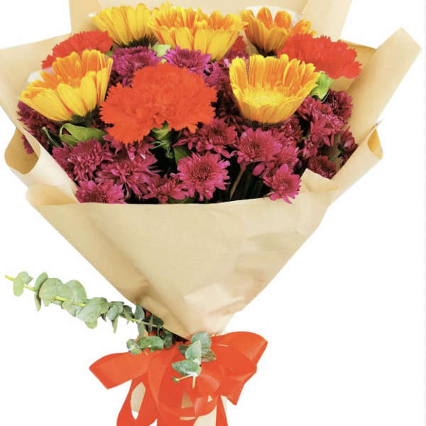 Bouquet of yellow, orange, and magenta flowers wrapped in tan paper with a red ribbon