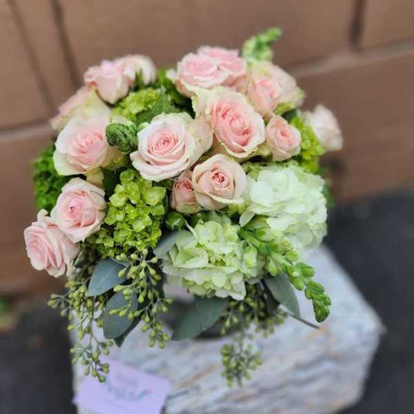 Round arrangement of pale pink roses with white and green hydrangeas in a clear glass vase