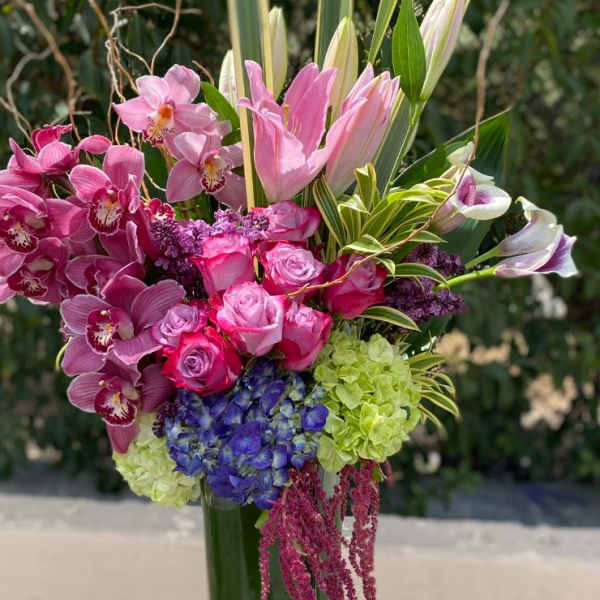Pink orchids, roses, lilies, and hydrangeas in a tall glass vase